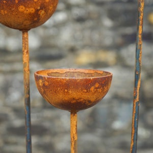 May include: A rusty metal garden sculpture with three round bowls. The bowls are attached to a metal stand with a rustic, weathered finish.