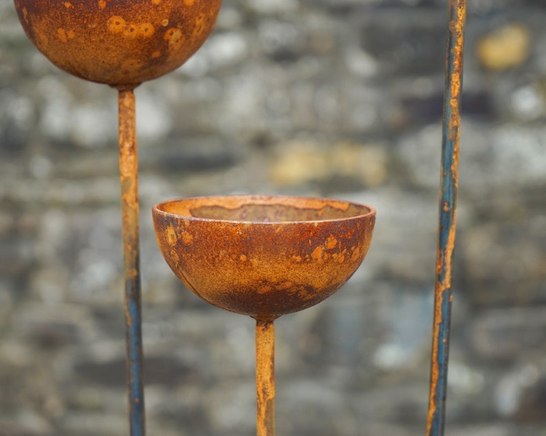 May include: A rusty metal garden sculpture with three round bowls. The bowls are attached to a metal stand with a rustic, weathered finish.