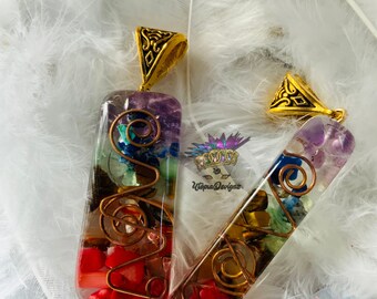 May include: Two rectangular resin pendants featuring embedded multi-colored gemstone chips and a copper wire spiral design. Each pendant has a gold-tone metal bail at the top. The text UtopiaDevignz is printed in the center between the pendants.