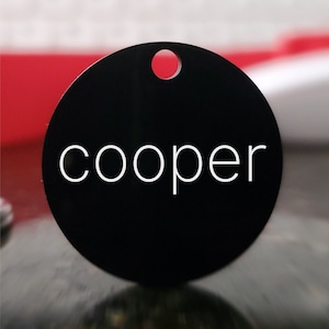 May include: Black round pet tag with a white hole at the top and the word "cooper" in white lettering.