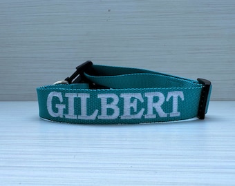 May include: Teal blue dog collar with white embroidered text that reads "GILBERT".