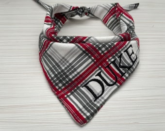 May include: A red and gray plaid dog bandana with the name "DUKE" embroidered in black thread.