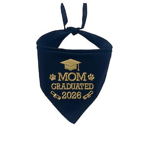May include: Navy blue pet bandana with gold embroidered text and graphics. The text reads "MOM GRADUATED 2026" with paw prints, a graduation cap, and diploma graphics. The bandana is tied at the top.