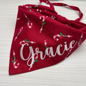 May include: Red Christmas dog bandana with a white candy cane pattern and the name "Gracie" embroidered in white.