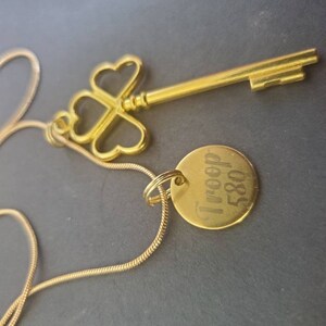 May include: A gold necklace with a key pendant and a round charm engraved with "I'm free" and "580".