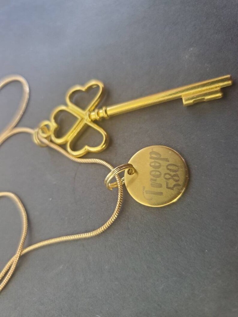 May include: A gold necklace with a key pendant and a round charm engraved with "I'm free" and "580".