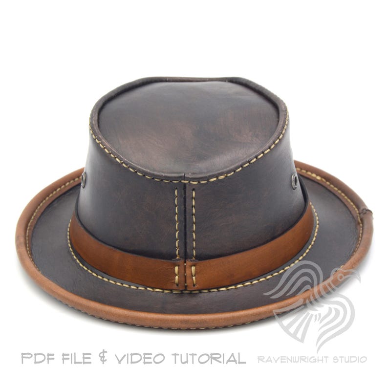 May include: A brown leather hat with a wide brim and a brown leather band. The hat has a structured crown and is stitched with light-colored thread. The brim is trimmed with a lighter brown leather. The text "PDF FILE & VIDEO TUTORIAL" is at the bottom.