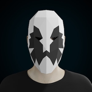 May include: A white paper mask with black geometric shapes forming a face. The mask has a sharp, angular design and appears to be made of folded paper.