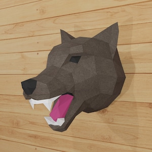 May include: A papercraft wolf head sculpture with a snarling expression. The wolf is made of gray paper and has a pink tongue. The sculpture is mounted on a wooden wall.