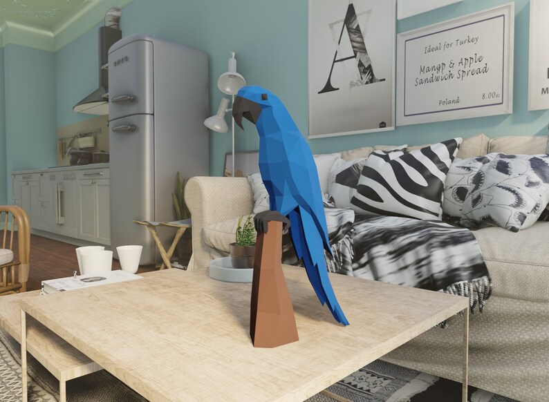 May include: A blue origami parrot perched on a brown wooden branch. The parrot is in a living room setting with a couch, coffee table, and a lamp.