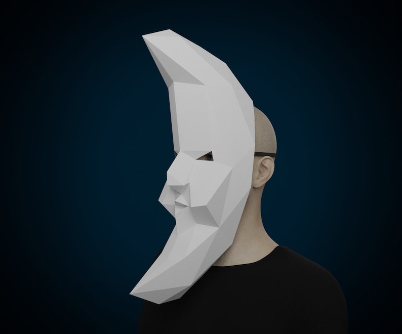 May include: A white paper mask shaped like a crescent moon. The mask is covering the face of a person wearing a black shirt.