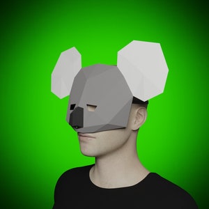 May include: A grey and white paper mask of a koala. The mask has a 3D effect and covers the person's face. The mask is worn by a person with a black shirt.