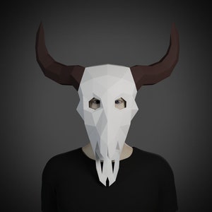 May include: A person wearing a white geometric paper mask in the shape of a bull skull with brown horns. The person is wearing a black shirt against a gray background. The mask has eye holes and a long, pointed jaw.