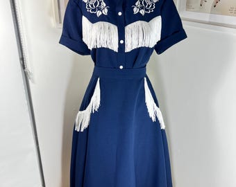May include: A navy blue midi dress featuring a collared neckline, short sleeves with cuffs, and a button-down front. The bodice and skirt are adorned with white fringe trim and white embroidered rose motifs on the chest area.