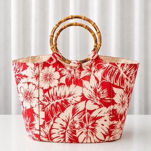 Peut inclure: Un sac fourre-tout arborant un motif floral et végétal tropical rouge vif sur fond blanc cassé. Le sac est doté de deux anses circulaires en bambou fixées sur le dessus, offrant une ouverture structurée pour le compartiment principal.