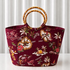 Peut inclure: Un sac fourre-tout bordeaux profond orné d'un imprimé tropical hawaïen avec des palmiers, des fleurs d'hibiscus et les noms des îles Oahu, Maui et Molokai. Le sac possède deux anses circulaires en bambou et une silhouette structurée.
