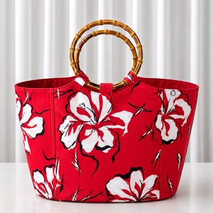 Peut inclure: Un sac fourre-tout rouge orné d'un motif floral blanc et noir avec deux anses circulaires en bambou. Le sac présente une ouverture large, une base structurée et un extérieur en tissu rouge vif décoré de grands motifs de fleurs blanches stylisées.