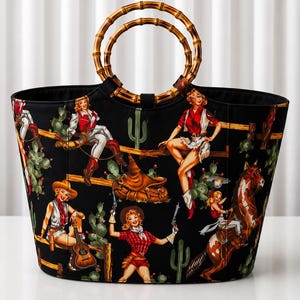 Peut inclure: Un sac fourre-tout noir orné d'un motif répétitif de cow-girls en tenue western, de cactus et de chevaux. Le sac possède deux anses circulaires en bambou fixées sur le dessus. Le tissu présente des personnages en rouge et blanc avec des selles.