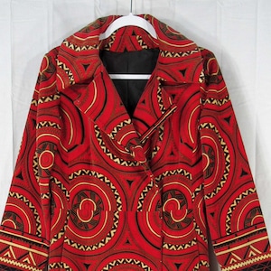 May include: A long red coat with a bold geometric pattern featuring concentric circles in black, brown, and gold. The coat has a notched collar, long sleeves, and a double-breasted design. The hem and sleeve cuffs have a decorative border.