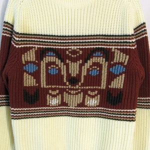 May include: Cream-colored knit sweater with a crew neck and long sleeves. The sweater features a geometric design in burgundy, black, tan, and blue across the chest. The sleeves and lower portion of the sweater are cream-colored.