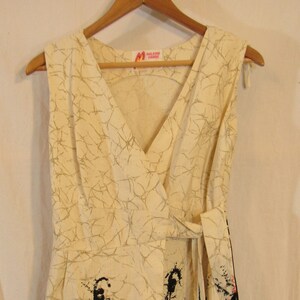 May include: A white sleeveless wrap dress with a black and red abstract print. The dress has a V-neckline and a tie at the waist. The label "Maldon Hawaii" is visible on the dress.