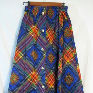 May include: A long, quilted skirt with a plaid pattern in shades of blue, orange, red, and green. The skirt has a button closure and a matching belt.