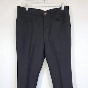 May include: Black dress pants with a button closure and two front pockets. The pants are hanging on a white hanger against a white background. The pants have a classic, straight-leg design.