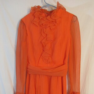 May include: A bright orange dress with a ruffled collar and long sleeves. The dress has a pleated skirt and a matching sash.