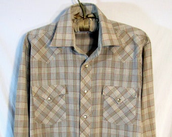 May include: A tan and red plaid button-up shirt with two chest pockets and gold-colored snaps. The long-sleeved shirt is hanging on a hanger. The shirt has a classic western style.