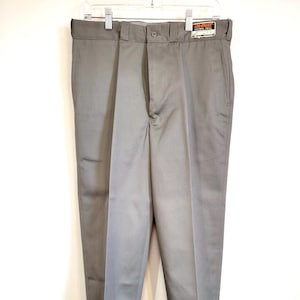 May include: Gray dress pants with a button closure and a tag. The pants are hanging on a white hanger. The pants have a straight leg and are cuffed at the bottom.