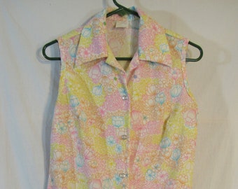 May include: Sleeveless button-down shirt with a floral pattern in pastel colors. The shirt features a collar and is adorned with small, silver-colored buttons. The floral design includes yellow, pink, blue, and white flowers.