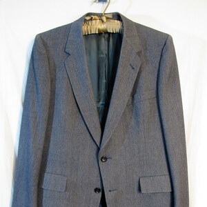May include: A gray blazer with a single-breasted closure and two button pockets. The blazer has a subtle herringbone pattern and a dark lining.