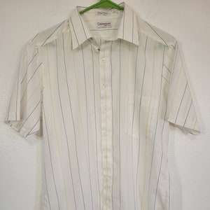 May include: White short-sleeve shirt with vertical stripes in yellow and navy blue. The shirt has a collared neckline, a chest pocket, and a button-down front. The brand name "Counterpoint" is visible on the label.