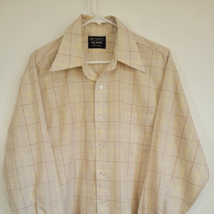 May include: A button-down, long-sleeve shirt in a plaid pattern of beige, yellow, and brown. The shirt has a wide collar and buttoned cuffs. The tag reads "NO IRON" and "JCPenney".