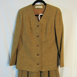 May include: A brown tweed skirt suit with a matching jacket and skirt. The jacket has a V-neck and five buttons down the front. The skirt is pleated and falls to the knee.