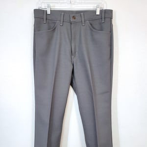 May include: Gray trousers hanging on a clear hanger. The pants have a button closure, belt loops, and front and back pockets. The fabric appears to be a solid color, with a slight sheen. The trousers are a classic, straight-leg style.