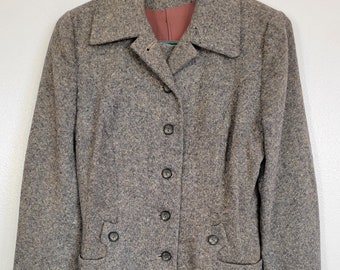 May include: A vintage two-piece suit in a speckled brown and gray tweed fabric. The jacket has a notched collar, four buttons, and two front pockets. The skirt is a simple, straight design. The suit is hanging on a green hanger.