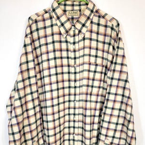 May include: Cream-colored plaid button-down shirt with a button-down collar. The shirt features a classic plaid pattern in cream, black, purple, and orange. The L.L. Bean label is visible on the upper chest. The shirt has long sleeves and buttoned cuffs.