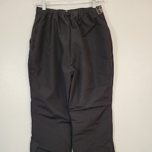 May include: Black ski pants with a drawstring waist and zippered pockets on the legs. The pants have a fleece lining and are made by the brand "Mountain Peak".