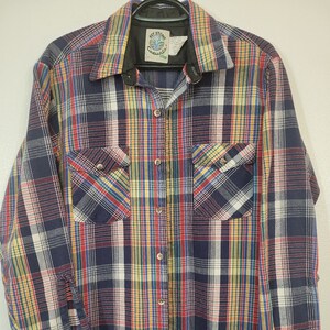 May include: A long-sleeved, button-down shirt with a plaid pattern in navy blue, red, yellow, and white. The shirt has two chest pockets and a collar. The label reads "Key Stone Casuals".