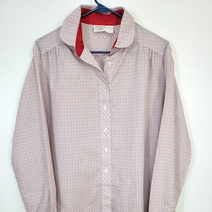 May include: A long-sleeved button-down shirt with a red and white plaid pattern. The shirt has a red collar lining and white buttons. The shirt is hanging on a blue hanger against a white background.