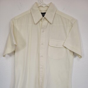 May include: A white short-sleeved button-down shirt with a single chest pocket. The shirt has a classic collar and a button closure.