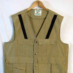 May include: A tan vest with multiple pockets and black straps. The vest has a V-neck and is buttoned down the front. The label reads "Ultimate Experience". The vest is hanging on a wooden hanger.