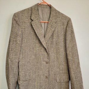 以下が含まれることがあります： シングルボタン留めのブラウンツイードブレザー。ブレザーは控えめなパターンとクラシックなフィット感です。