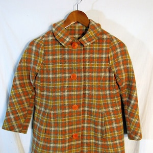 May include: A vintage plaid coat in orange, yellow, and gray. The coat features a collared neckline, three orange buttons, and two front pockets. The coat is hanging on a wooden hanger.