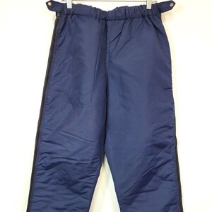 May include: Navy blue sweatpants with a drawstring waist and zippered side panels. The sweatpants have a cuffed bottom.