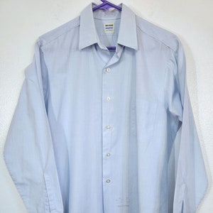 May include: A light blue long-sleeved button-down shirt with a white pocket on the left side. The shirt has a white label with the text "Van Heusen" and "Comfort Flex" on it.