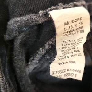 Puede incluir: Primer plano de una prenda de mezclilla negra con una etiqueta blanca. La etiqueta muestra texto que incluye "NA702BK", "5/6 X 36" y "100% COTTON". La etiqueta tambi&eacute;n incluye instrucciones de lavado y "MADE IN USA".