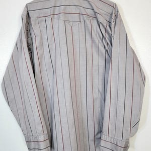 May include: A gray button-down shirt with vertical stripes in black and burgundy. The long-sleeved shirt has a pointed collar and buttoned cuffs. The back of the shirt is visible, showing a yoke detail.