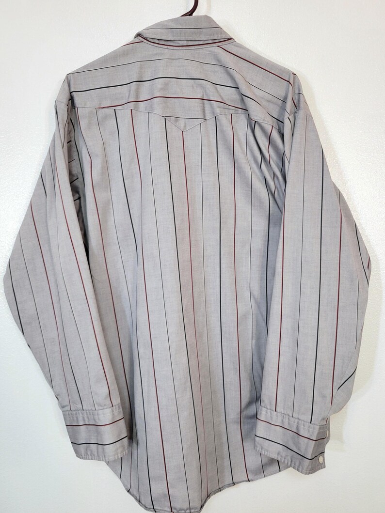 May include: A gray button-down shirt with vertical stripes in black and burgundy. The long-sleeved shirt has a pointed collar and buttoned cuffs. The back of the shirt is visible, showing a yoke detail.